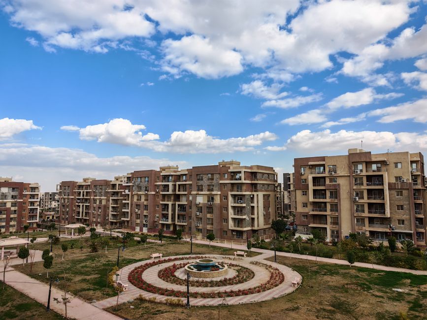 Aerial view of a modern residential complex with a central fountain under a blue sky