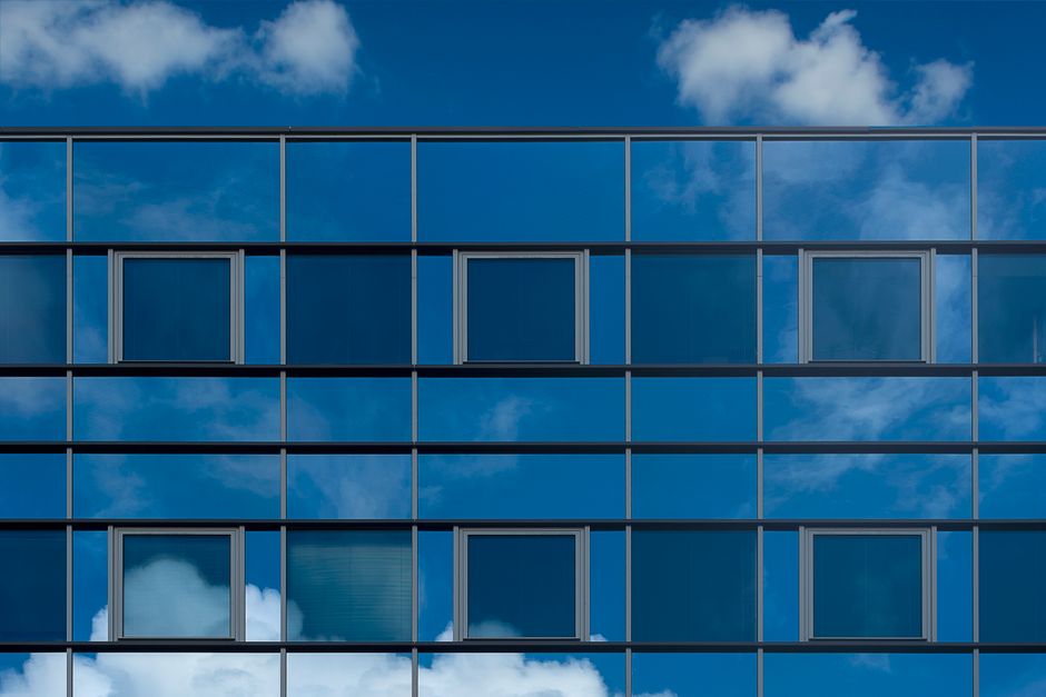 Facade of a modern glass building reflecting the blue sky and clouds